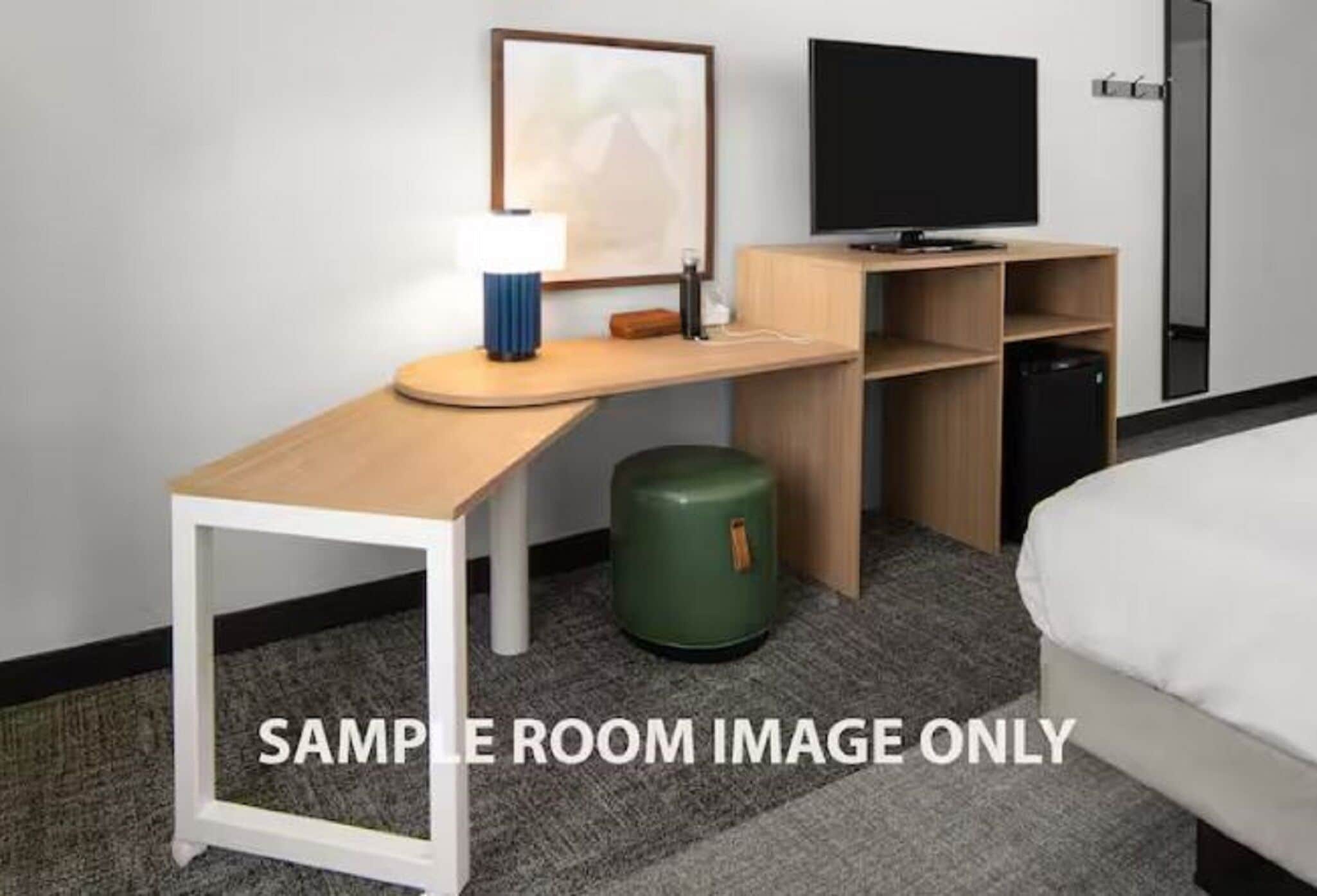 A hotel room with a bed, a desk with a lamp, a television, and a trash bin.