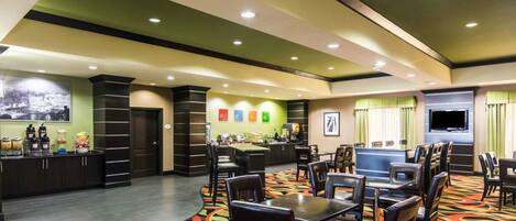 A hotel lobby with a buffet area, seating arrangements, and a television screen.