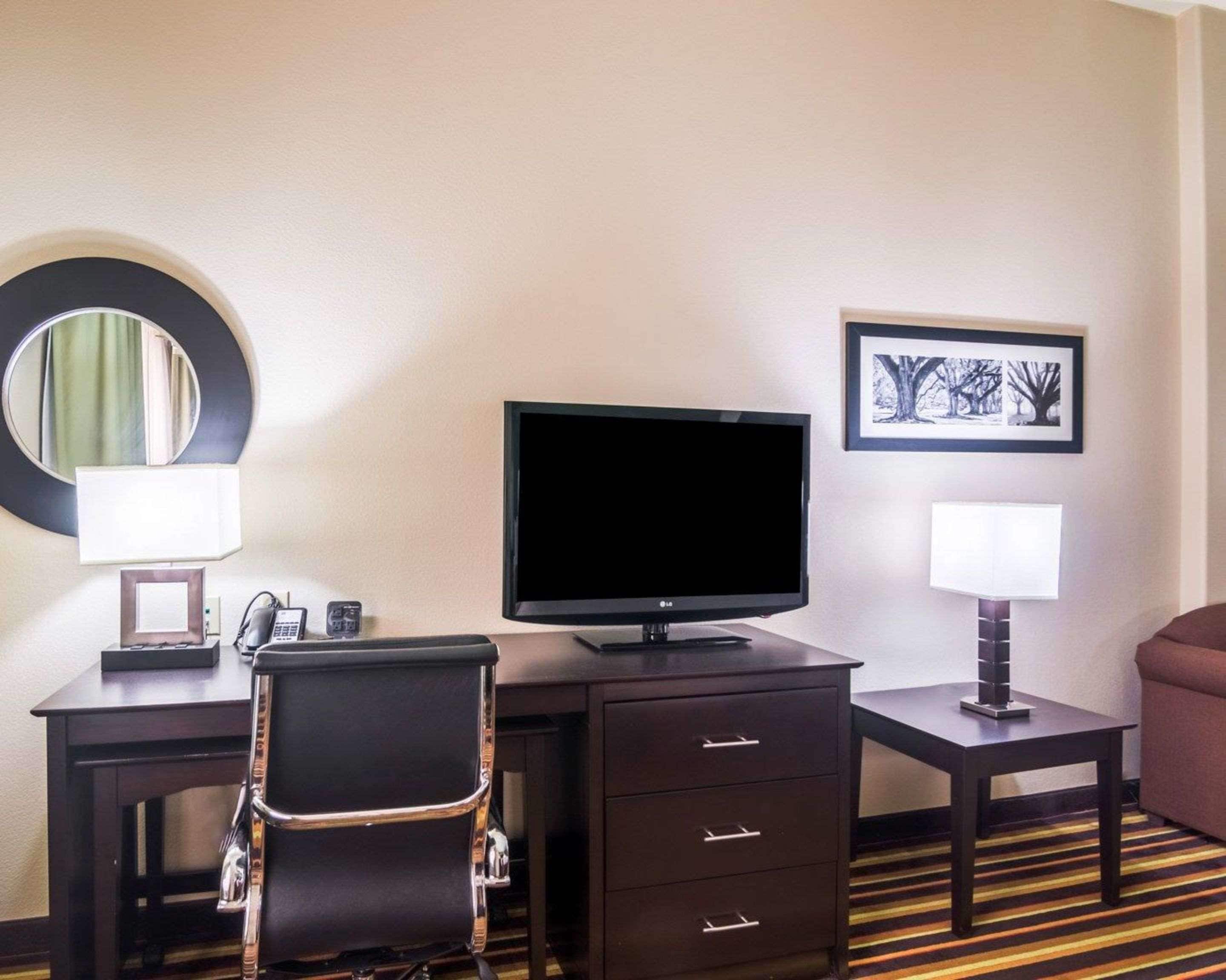 Une chambre d’hôtel équipée d’un bureau, d’une chaise, d’une télévision, d’une lampe, d’un tableau encadré et d’un canapé.