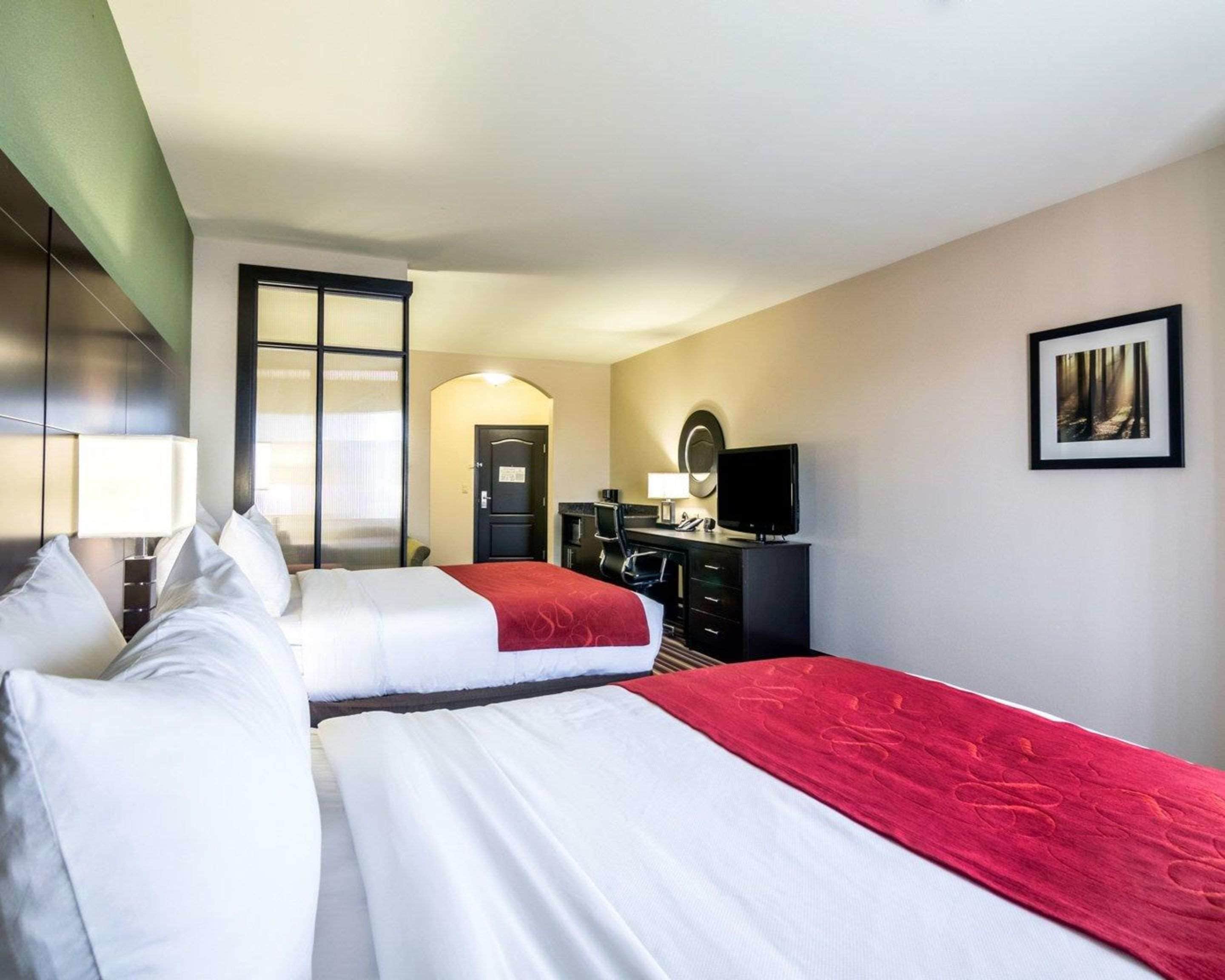 A hotel room with two beds, a desk with a TV, a mirror, and a framed picture on the wall.