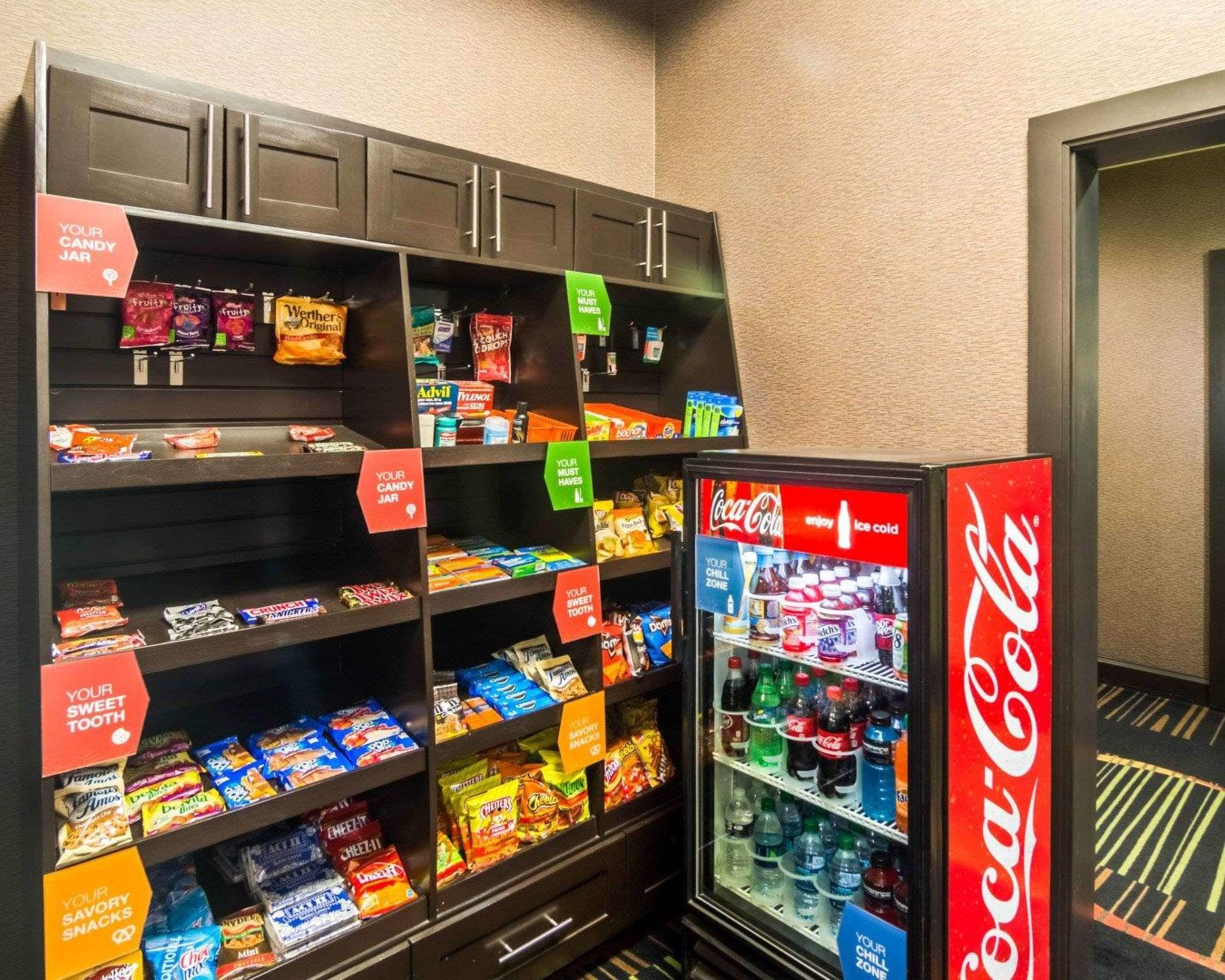 Un présentoir rempli de diverses confiseries et barres chocolatées, un réfrigérateur à boissons Coca-Cola et un meuble avec des tiroirs.