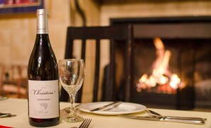 A bottle of Cristina 2016 Chardonnay and a wine glass on a table with a fireplace in the background. - Gooderson Kloppenheim Country Estate (eNtokozweni)