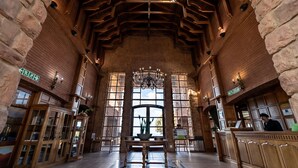 A lobby with a high ceiling, wooden beams, stone walls, and a central table with a chandelier. - Gooderson Kloppenheim Country Estate (eNtokozweni)