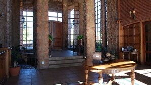 A spacious lobby with a high ceiling, large windows, and a central wooden table. - Gooderson Kloppenheim Country Estate (eNtokozweni)