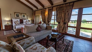 A spacious room with a bed, sofa, and armchairs, large windows with curtains, and a view of the outdoors. - Gooderson Kloppenheim Country Estate (eNtokozweni)