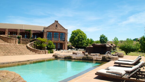 A pool area with lounge chairs, a stone building, and a staircase leading to a second floor. - Gooderson Kloppenheim Country Estate (eNtokozweni)