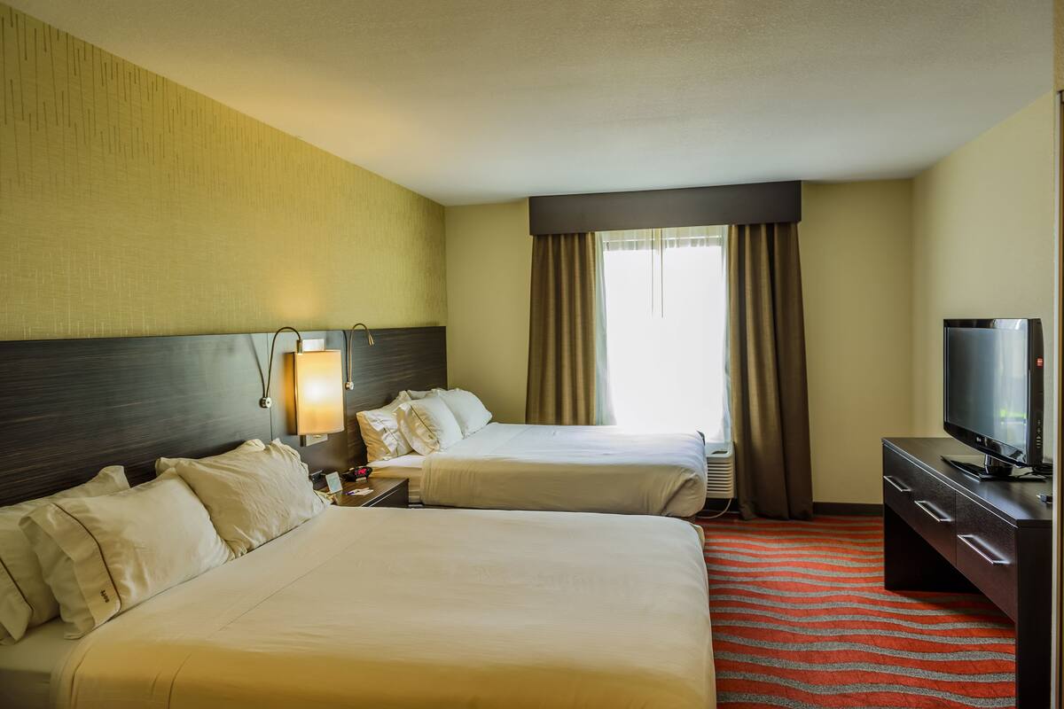 A hotel room with two beds, a TV, and a desk.