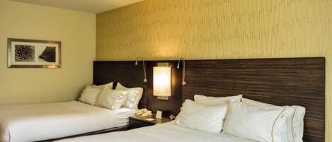 A hotel room with two beds, a nightstand, a wall-mounted lamp, and a framed picture.