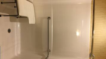 Un baño con bañera blanca, barras de apoyo, panel de control de ducha y suelo de madera.