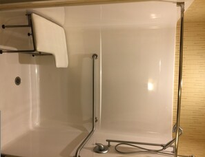 A bathroom with a white bathtub, grab bars, a shower control panel, and a wooden floor. - Holiday Inn Express Bradford by IHG (Bradford)