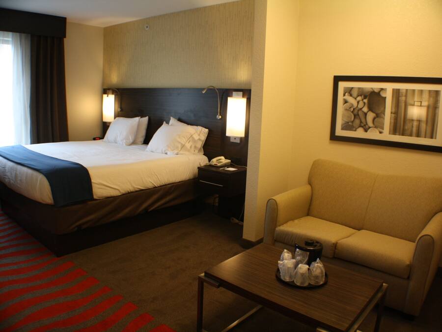 A hotel room with a large bed, a sofa, a coffee table, and a painting on the wall.
