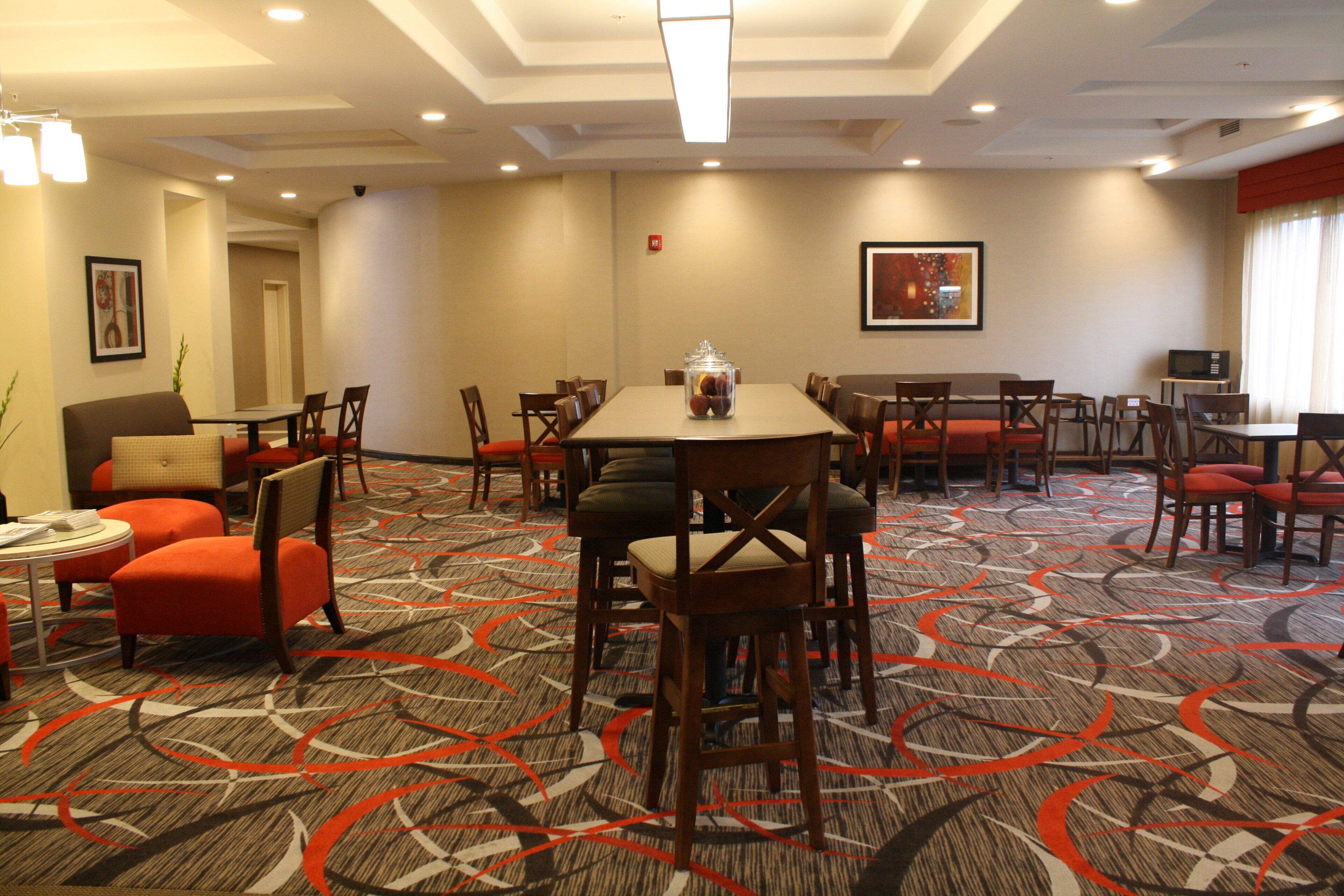 A hotel dining area with multiple tables and chairs, a fire extinguisher on the wall, and a framed picture above one of the tables.