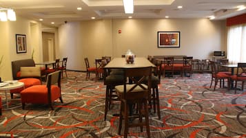 A hotel dining area with multiple tables and chairs, a fire extinguisher on the wall, and a framed picture above one of the tables.