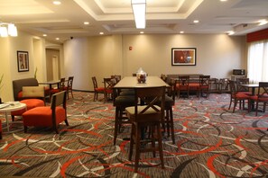 A hotel dining area with multiple tables and chairs, a fire extinguisher on the wall, and a framed picture above one of the tables.