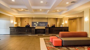 A hotel reception area with two reception desks, a waiting area with a sofa and ottoman, and a carpeted floor.