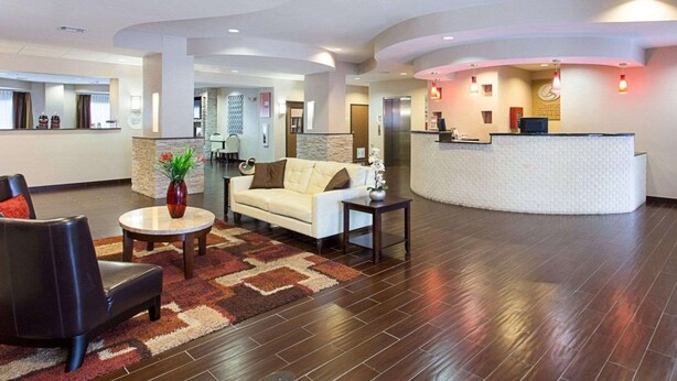 Un vestíbulo de hotel con una recepción, un sofá, una silla y una mesa de centro.