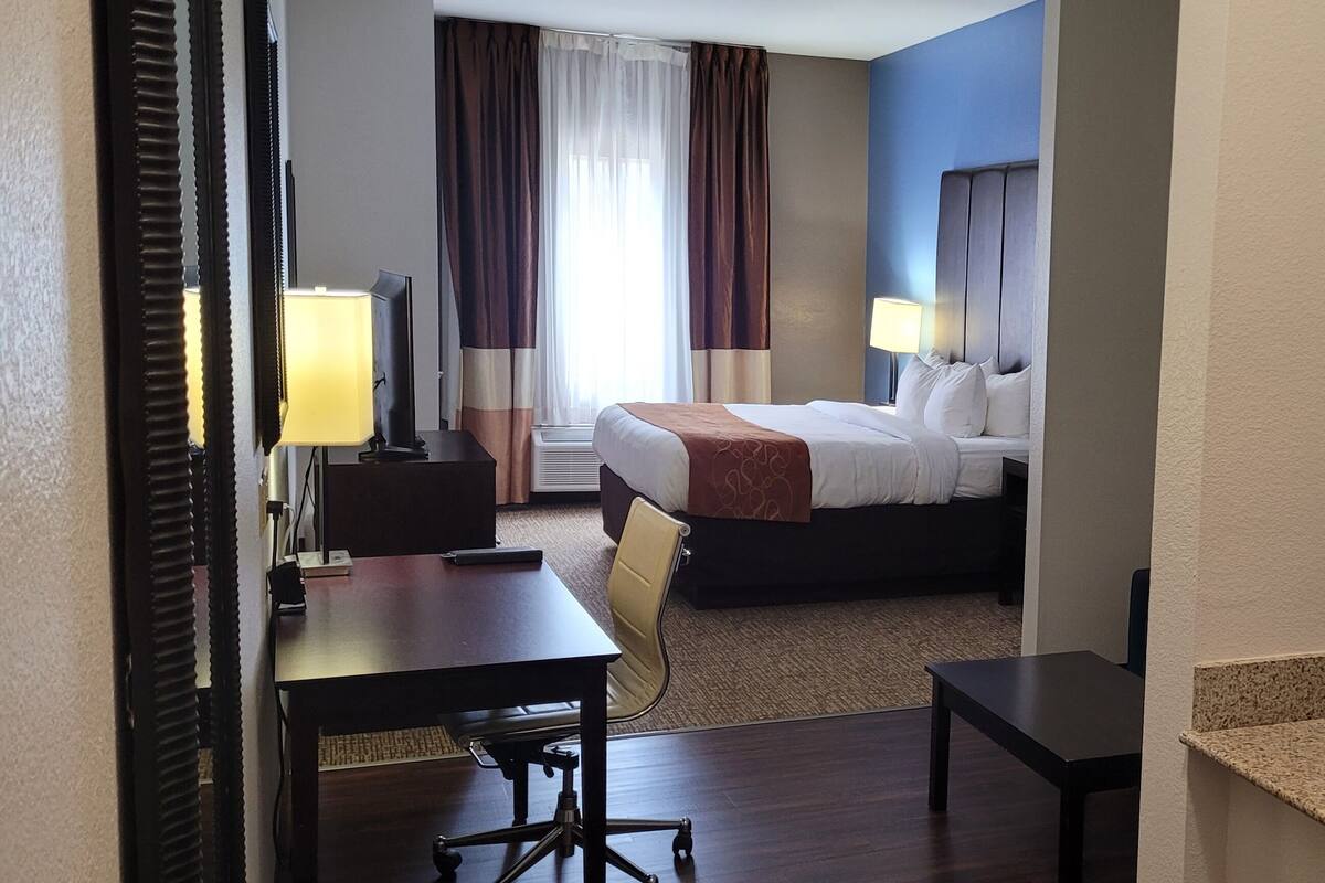 A hotel room with a bed, a desk, a chair, a TV, and a microwave.