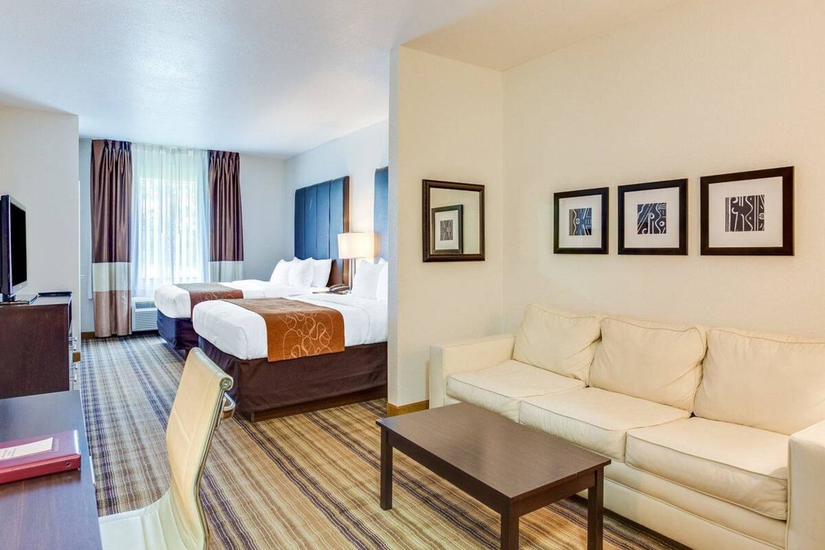 A hotel room with a bed, a sofa, a coffee table, a TV, and framed pictures on the wall.
