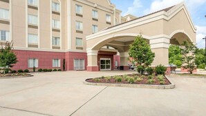 Un hotel con una entrada central, varios pisos y un patio ajardinado.