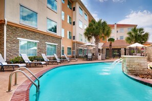 A swimming pool with lounge chairs and umbrellas, surrounded by a stone wall and a building with multiple windows and balconies. - Residence Inn Houston I-10 West/Park Row (Houston)