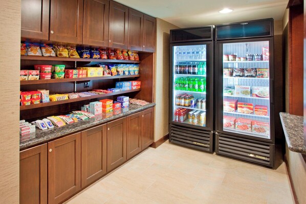 A self-service snack and beverage area with refrigerated cases and shelves stocked with various food items and drinks.