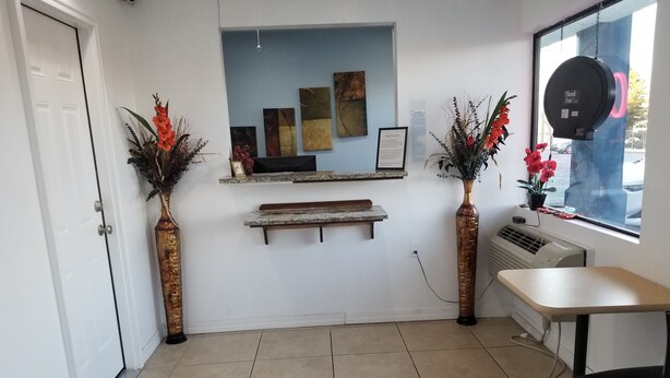 A reception area with a tiled floor, a reception desk, two vases with flowers, framed artwork on the wall, and a window with a view of the outside. - Nights Stay Hotel (Tulsa)