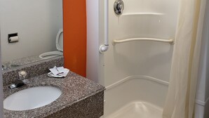 A bathroom with an orange wall, a white sink, and a walk-in shower with a curtain. - Nights Stay Hotel (Tulsa)