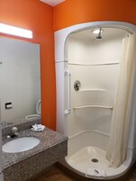 Un baño con una pared naranja, un lavamanos blanco y una ducha a pie con cortina.