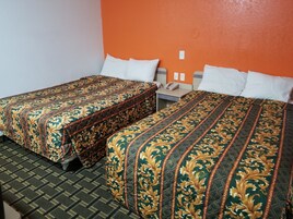 Una habitación de hotel con dos camas, cada una con una colcha estampada, una mesita de noche pequeña con un teléfono y un enchufe de pared.