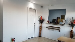 A hallway with a white door, a fire extinguisher, a potted plant, and a mirror on the wall. - Nights Stay Hotel (Tulsa)