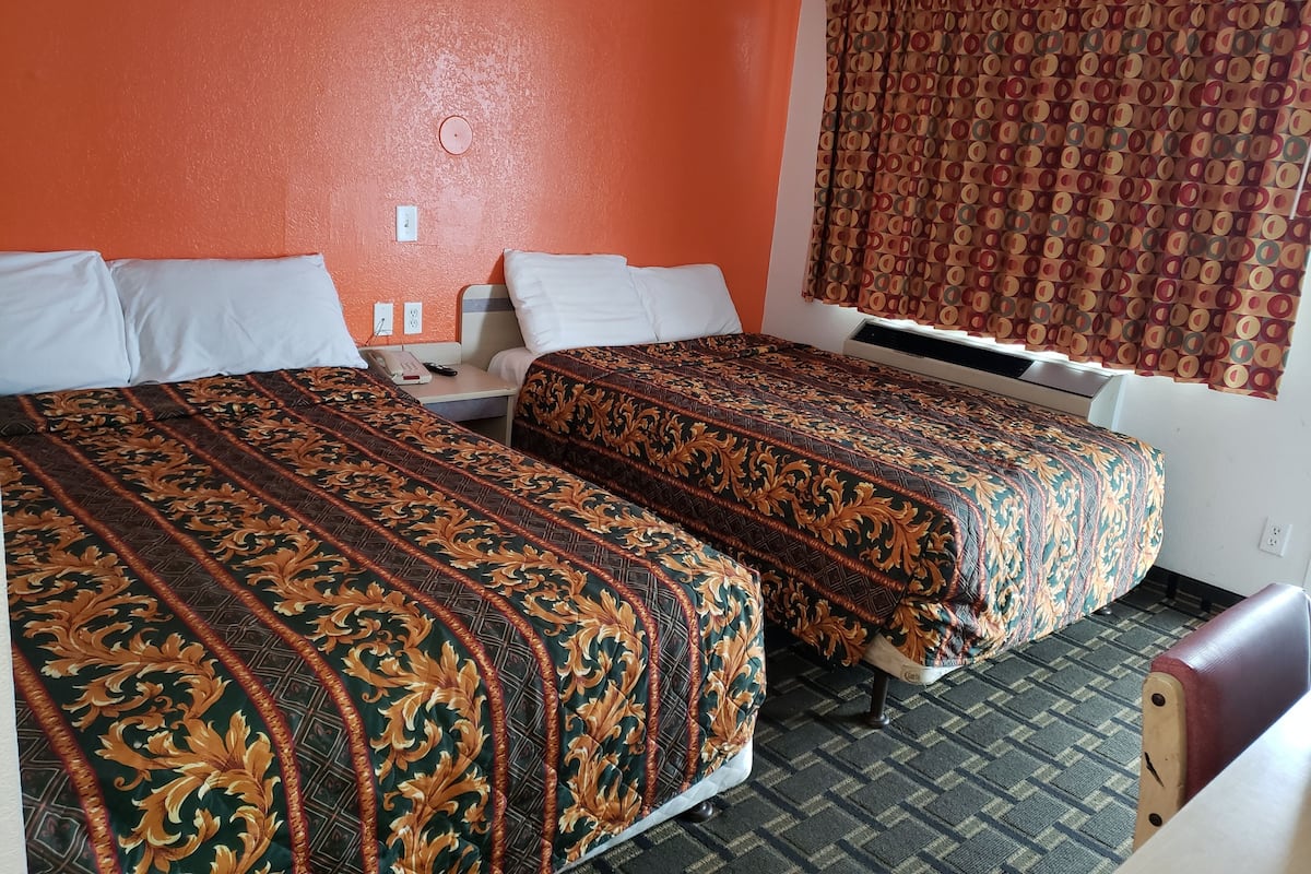 Ein Hotelzimmer mit zwei Betten, einem Nachttisch, einem Telefon und einem Fenster mit gemusterten Vorhängen.