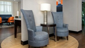 A hotel lobby with two grey upholstered chairs, a round table with a lamp, and a large window with curtains. - Hampton Inn Knoxville/Clinton I-75 (Clinton)