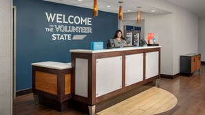 A reception desk with a blue wall and a welcome sign, a counter with a phone, and a minibar. - Hampton Inn Knoxville/Clinton I-75 (Clinton)