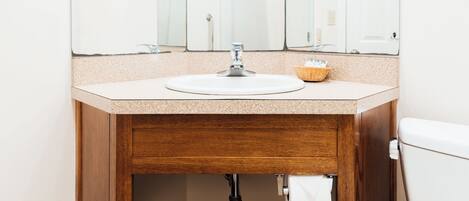 A bathroom with a wooden vanity, a sink, a mirror, and a toilet.