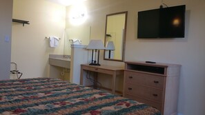 A hotel room with a bed, a dresser, a mirror, a television, and a bathroom with a sink and towel rack. - Rodeway Inn Kansas City Downtown Area (Kansas City)