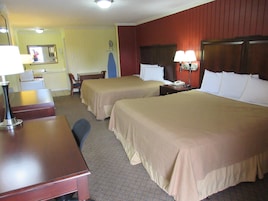 A hotel room with two beds, a desk, a chair, a telephone, and a mirror.