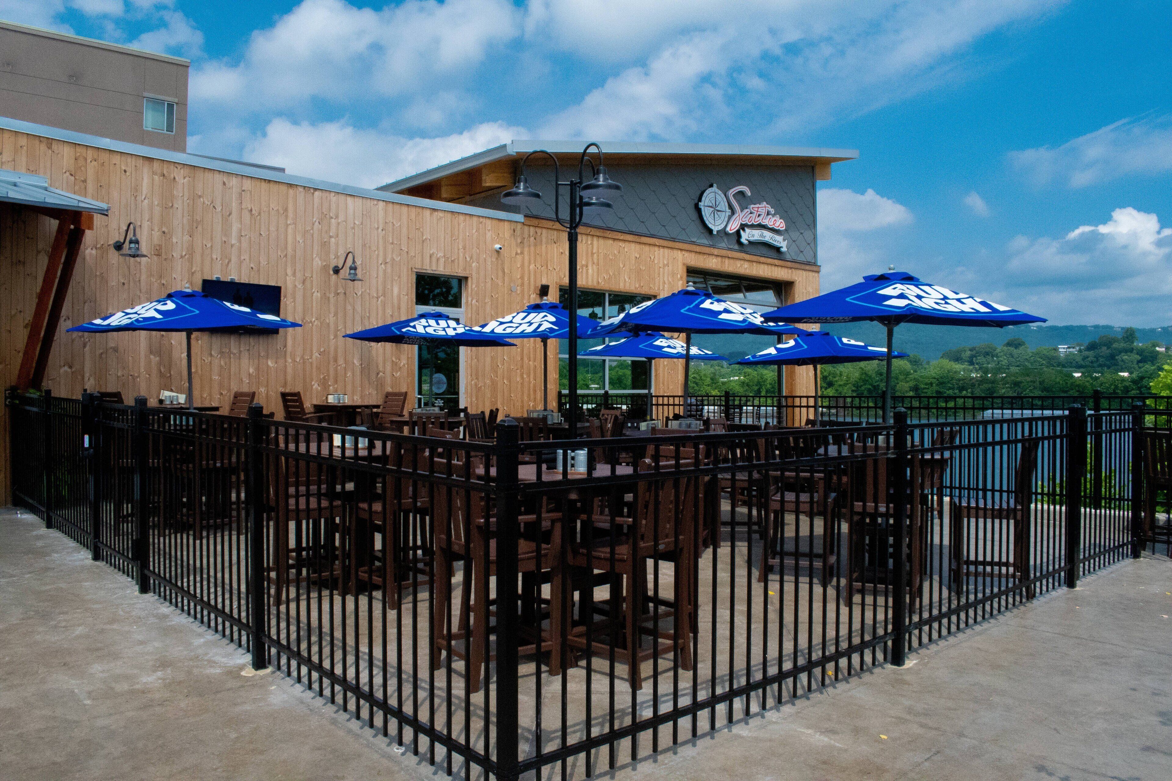 An outdoor seating area with tables and chairs, blue umbrellas, and a wooden fence.