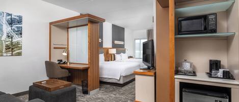 A hotel room with a bed, a desk with a chair, a television, a microwave, and a refrigerator.