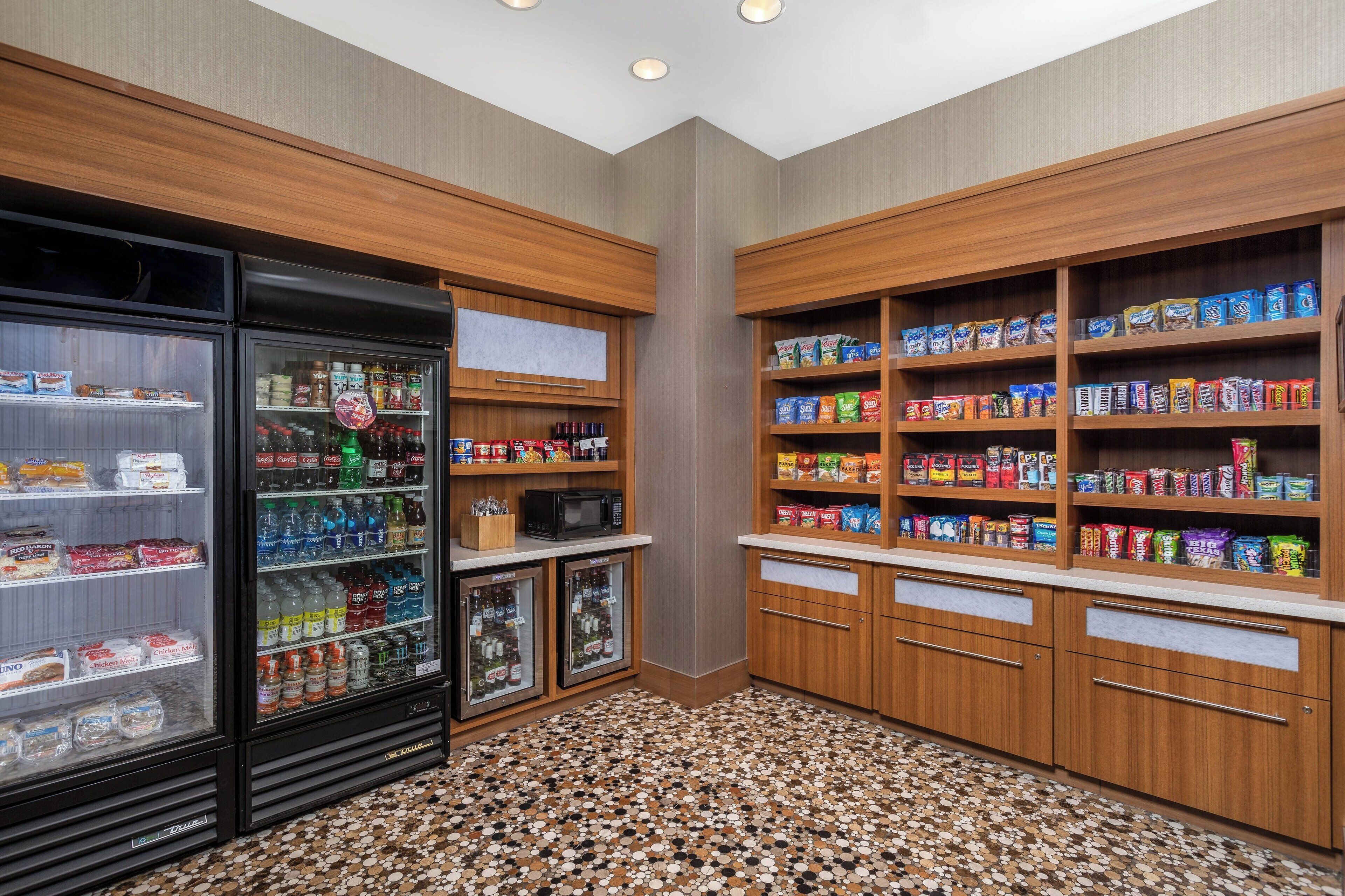A self-service snack area with refrigerated and non-refrigerated beverage dispensers, shelves stocked with snacks, and a microwave.