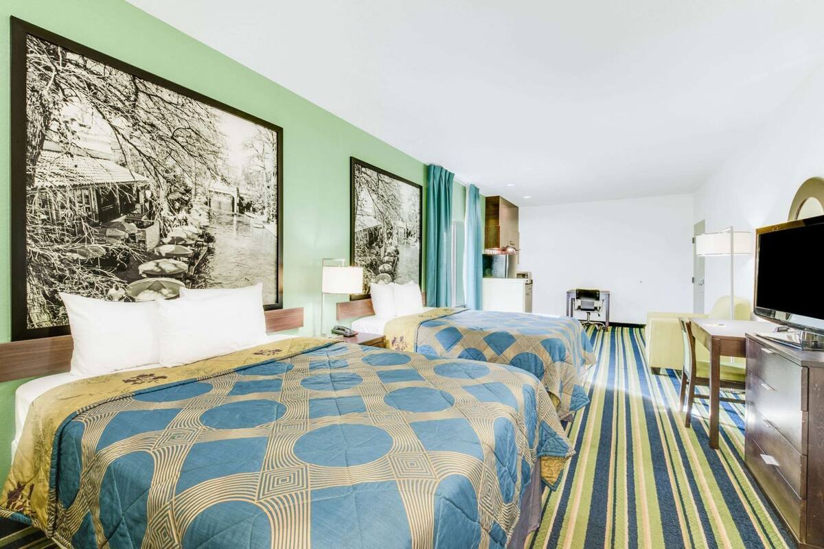 A hotel room with two beds, a desk, a television, and a large framed picture on the wall.