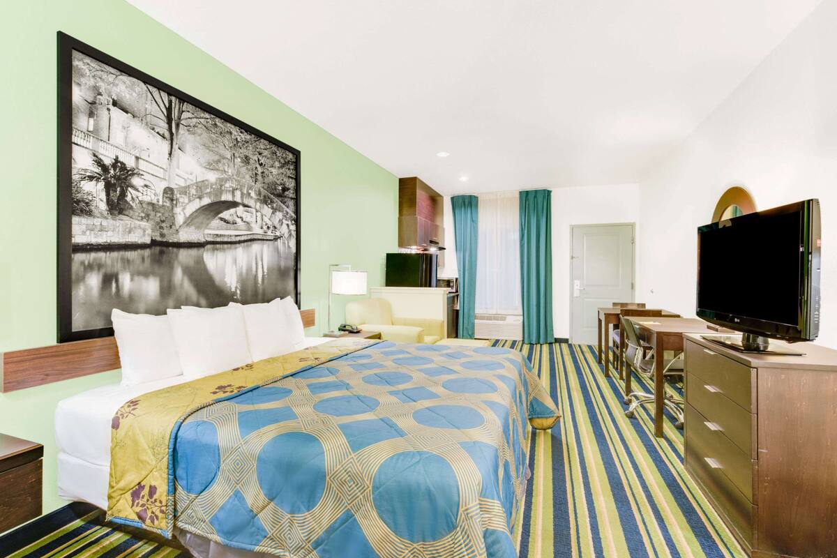 A hotel room with a bed, a desk, a television, and a large painting on the wall.