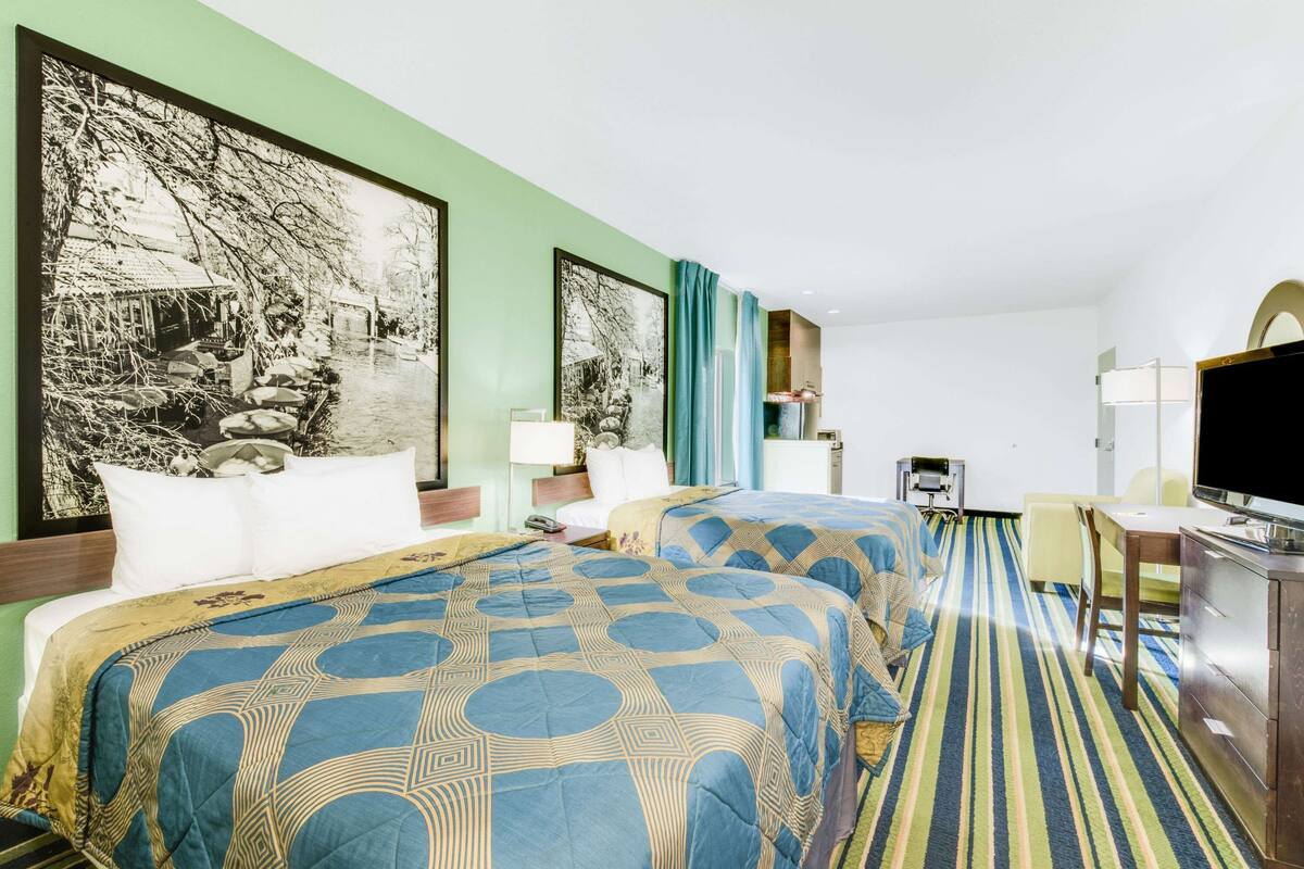 A hotel room with two beds, a desk, a television, and artwork on the walls.