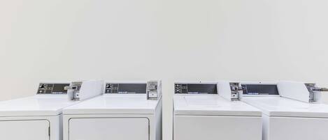 A row of white, identical laundry machines in a clean, empty room with a plain wall.
