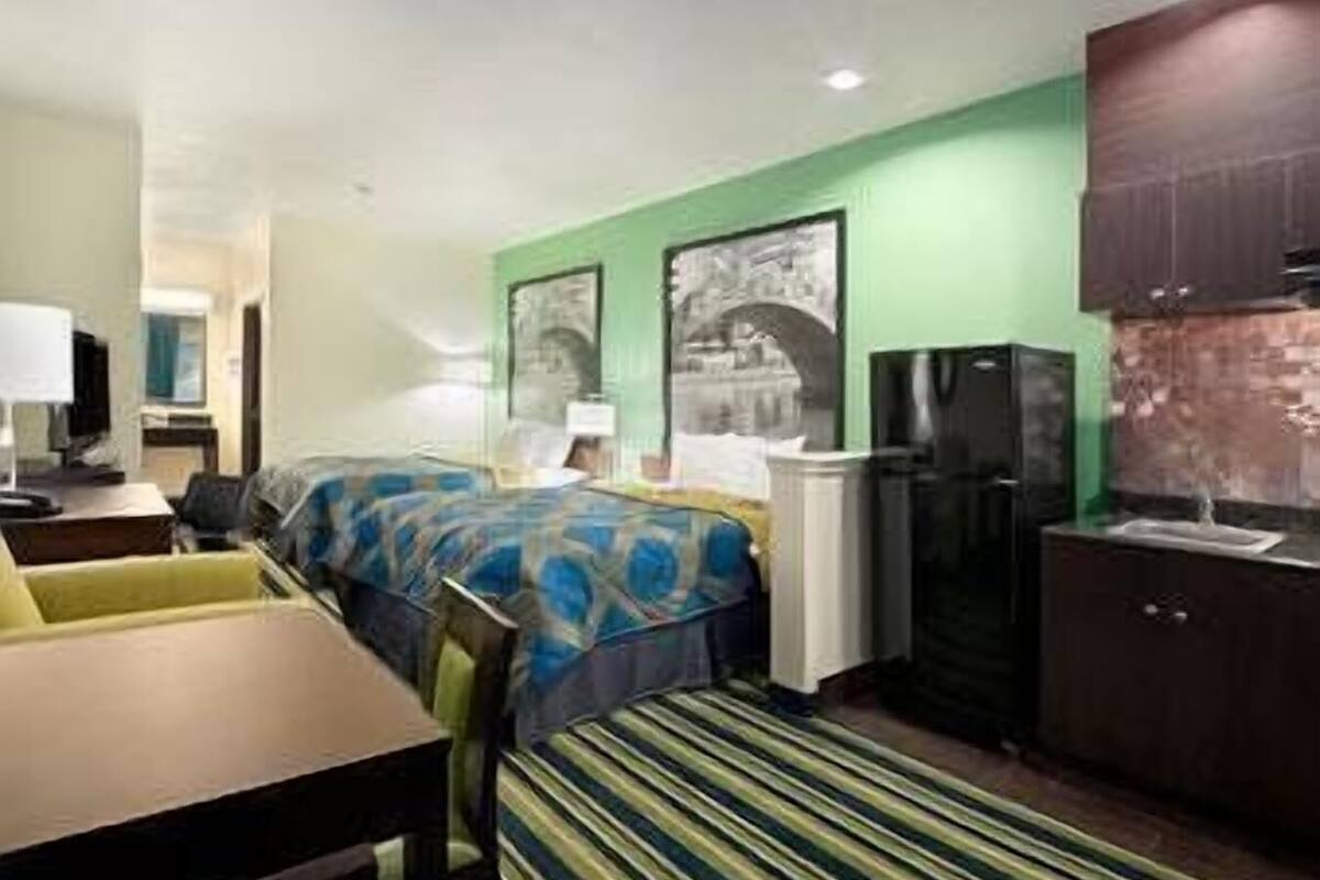 A hotel room with a bed, a desk, a chair, a television, a refrigerator, and a window.