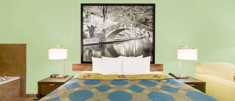 Habitación de hotel con una cama, dos mesitas de noche, una silla y un cuadro grande enmarcados con una imagen de un puente sobre el agua.