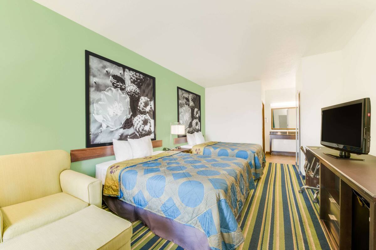 A hotel room with two beds, a TV, a sofa, and artwork on the walls.