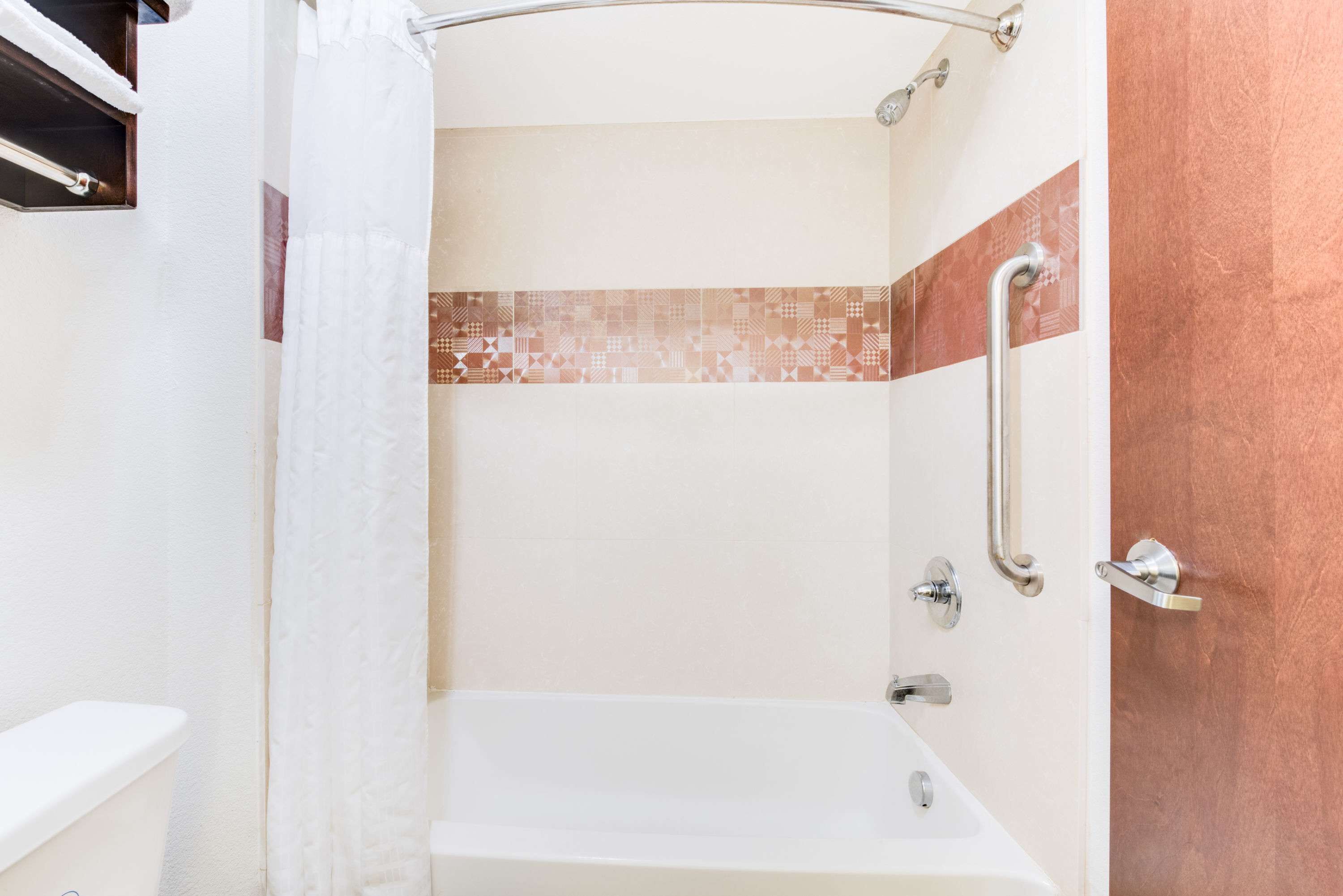 A shower with a white curtain, a handrail, and a tiled wall.