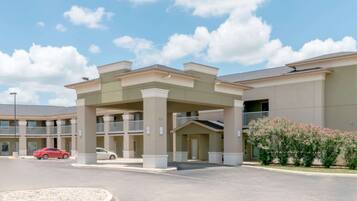 A hotel entrance with a covered walkway, multiple balconies, and a parking area with cars.
