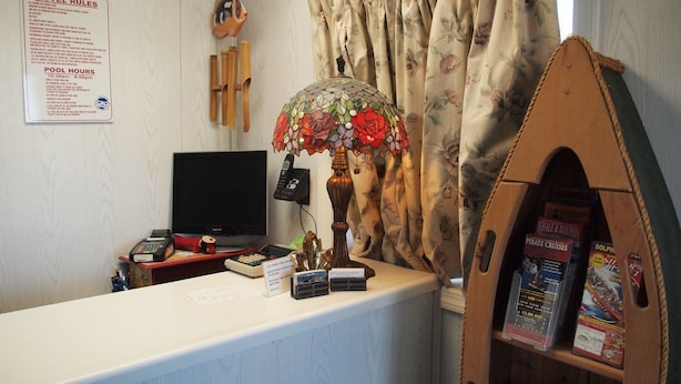 Una recepción con un cartel que detalla las normas del motel, un televisor, un teléfono, una lámpara decorativa y una estantería con libros.