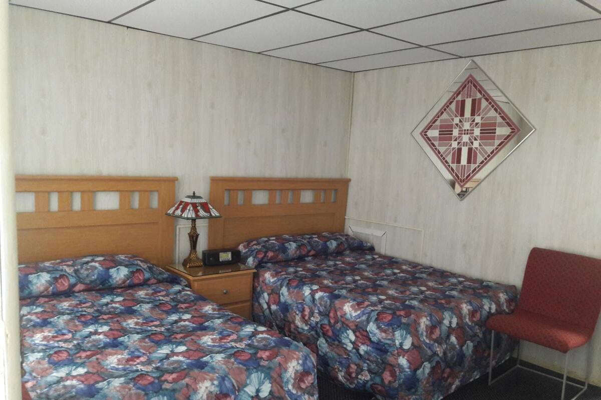 A hotel room with two beds, a nightstand, a lamp, a red chair, and a decorative wall piece.